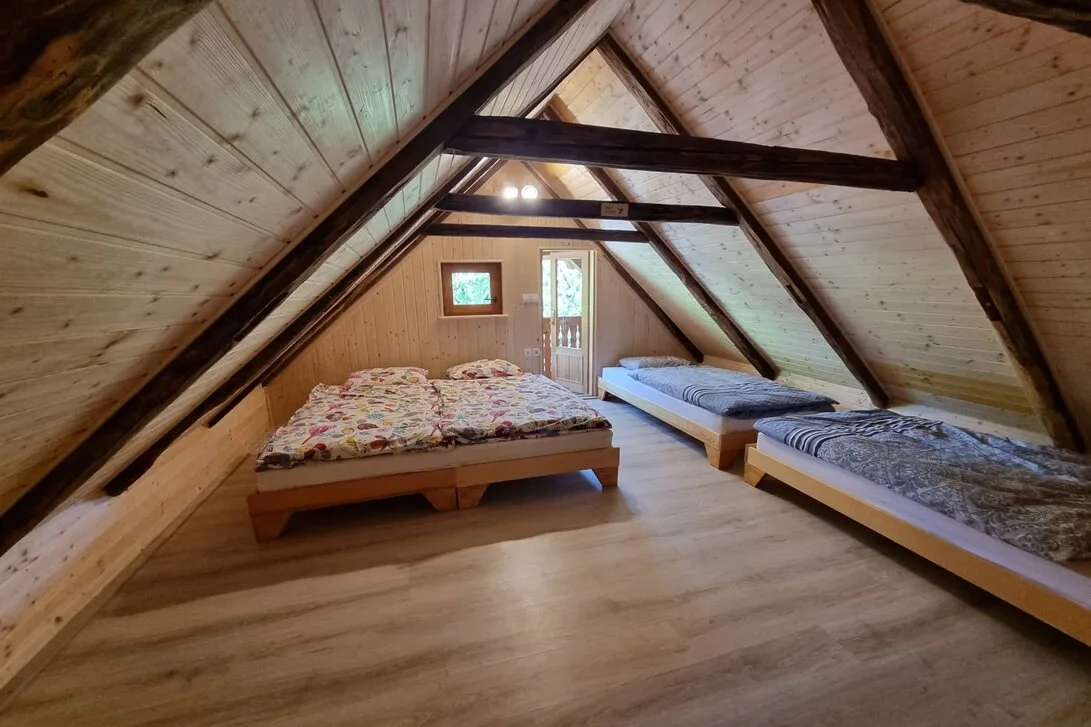 Podstrešna spalnica pod lesenimi tramovi z zakonsko posteljo in dvema enojnima posteljama